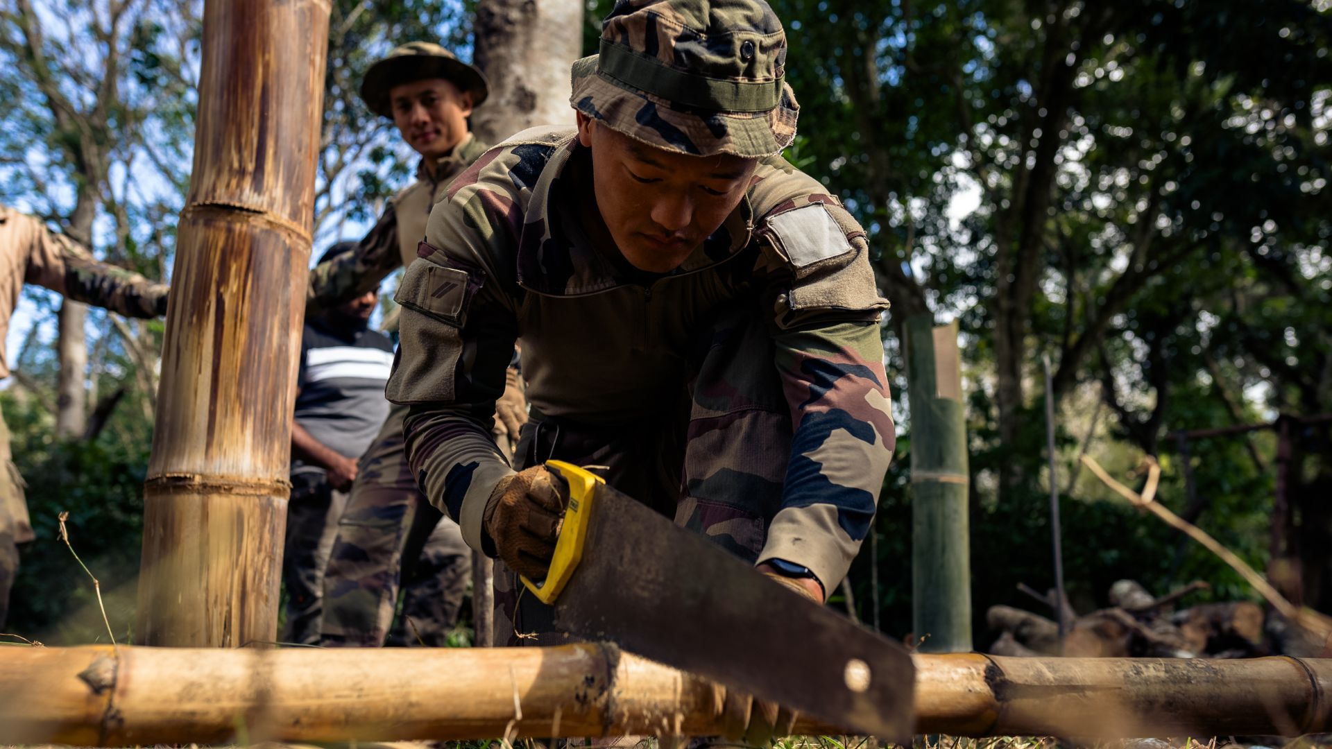 Le légionnaire découpe du bambou à l'aide d'une scie.