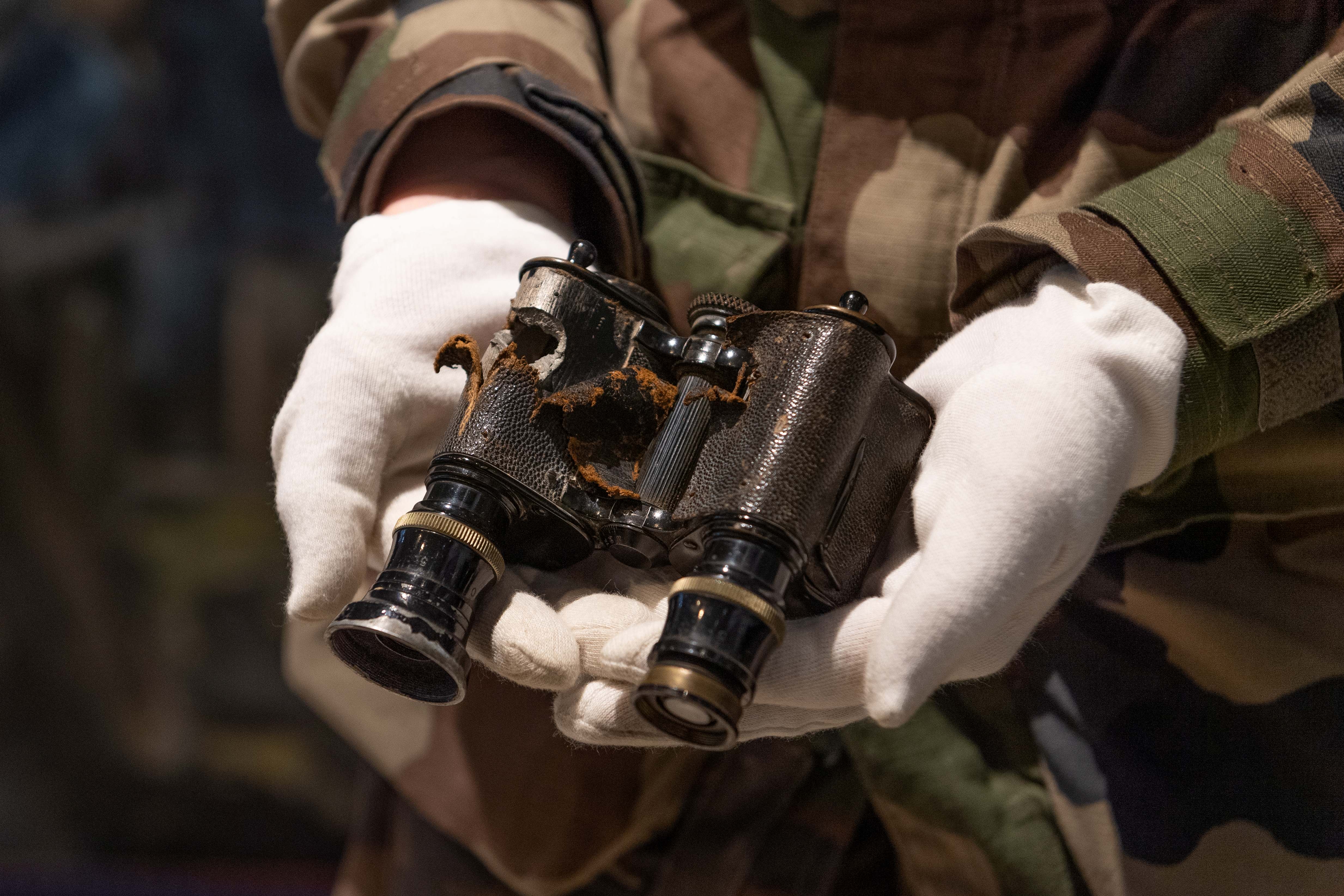 Des jumelles, trouée d'une balle pendant la seconde Guerre Mondiale, est présentée par une guide de visite.